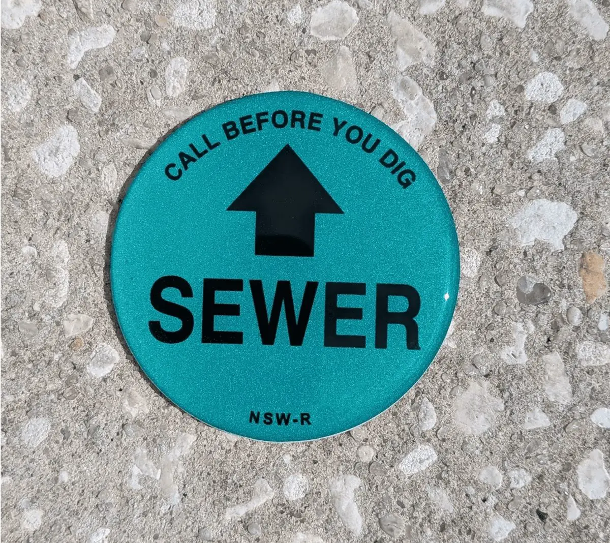 Sewer warning marker on concrete surface.