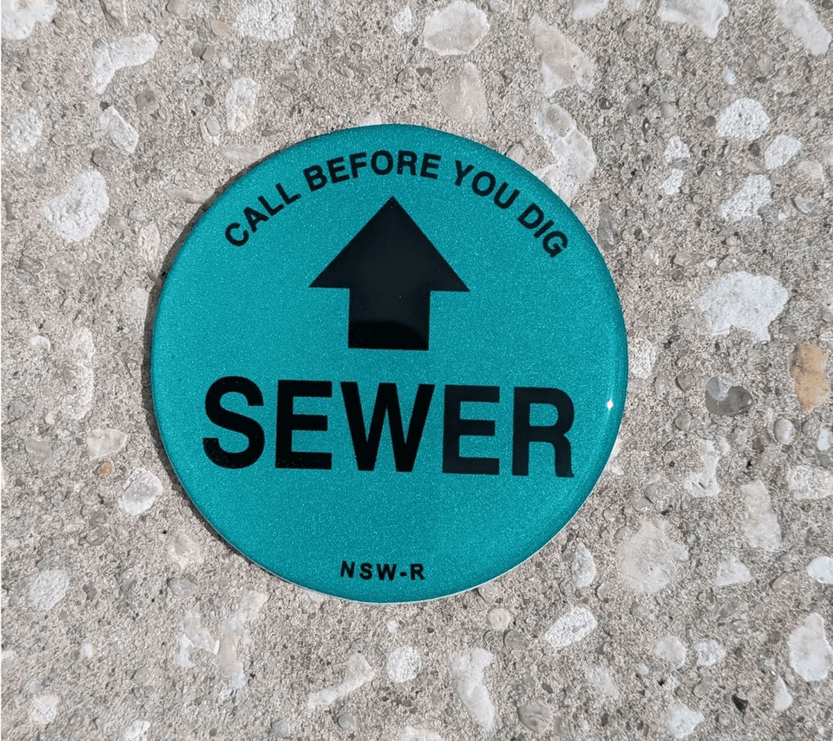Sewer warning marker on concrete surface.