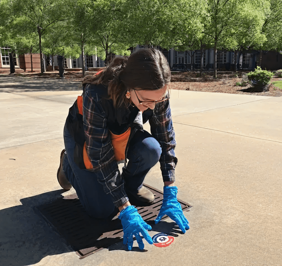Person installing a sticker on storm drain.