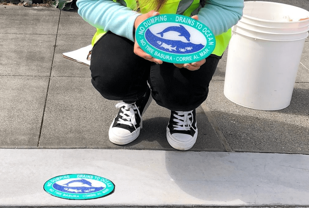 Person placing "No Dumping" sign on ground.