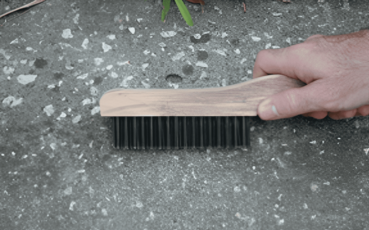 Hand scrubbing concrete surface with brush.